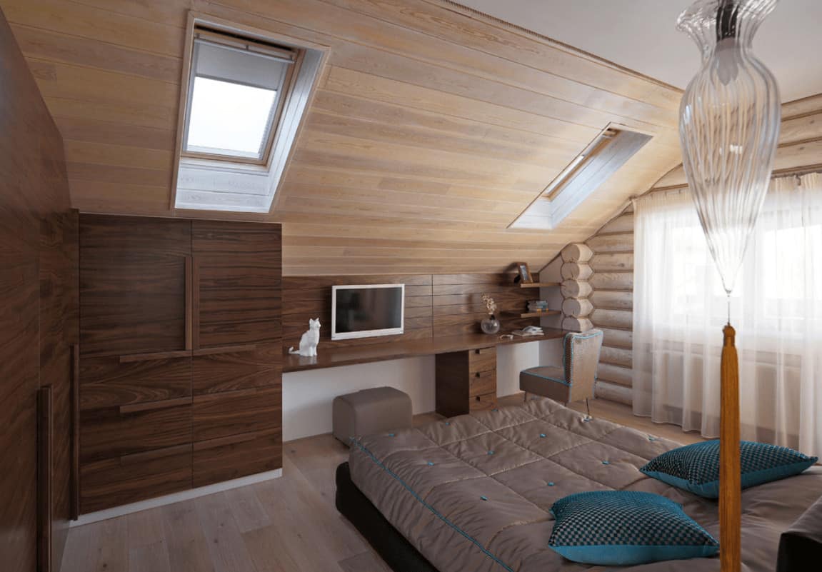 A cozy bed faces the built-in desk in this primary bedroom with floor to ceiling cabinets and a vaulted wall clad in light wood planks and fitted with skylight windows.