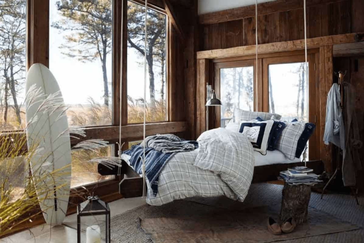 Natural light flows in through the glass paneled windows in this rustic bedroom offering a hanging bed and a stump coffee table that sits on layered rugs.