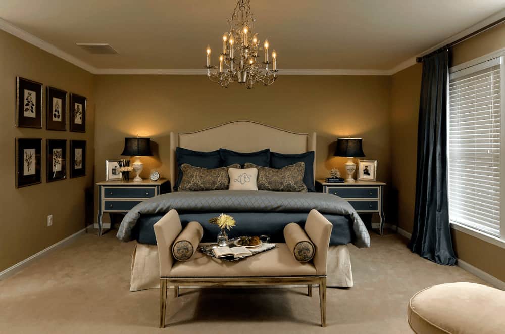 Classic brown primary bedroom decorated with gallery frames and a fancy chandelier that hung over the wingback bed flanked by blue nightstands and traditional table lamps.
