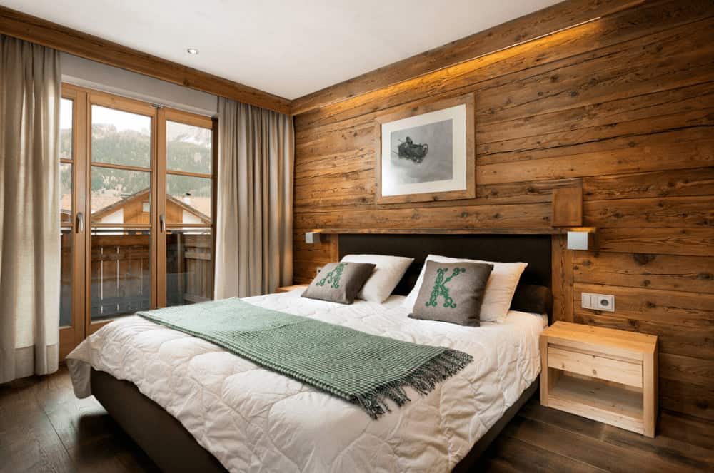 A green checkered throw blanket lays on the comfy bed with a framed artwork on top. It is situated in between wooden nightstands and sleek sconces.