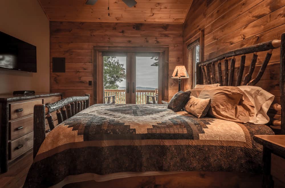 A log branch bed complements the drawer chest in this warm primary bedroom with a flat screen TV and table lamps that sit on wooden nightstands.