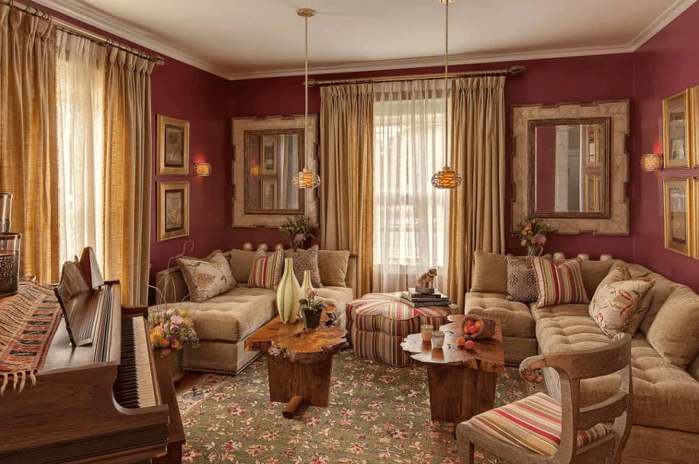 A baby grand piano and cozy seats surround a pair of stump coffee tables lighted by matching brass pendants. This room is decorated with framed mirrors and artworks mounted on the red walls.