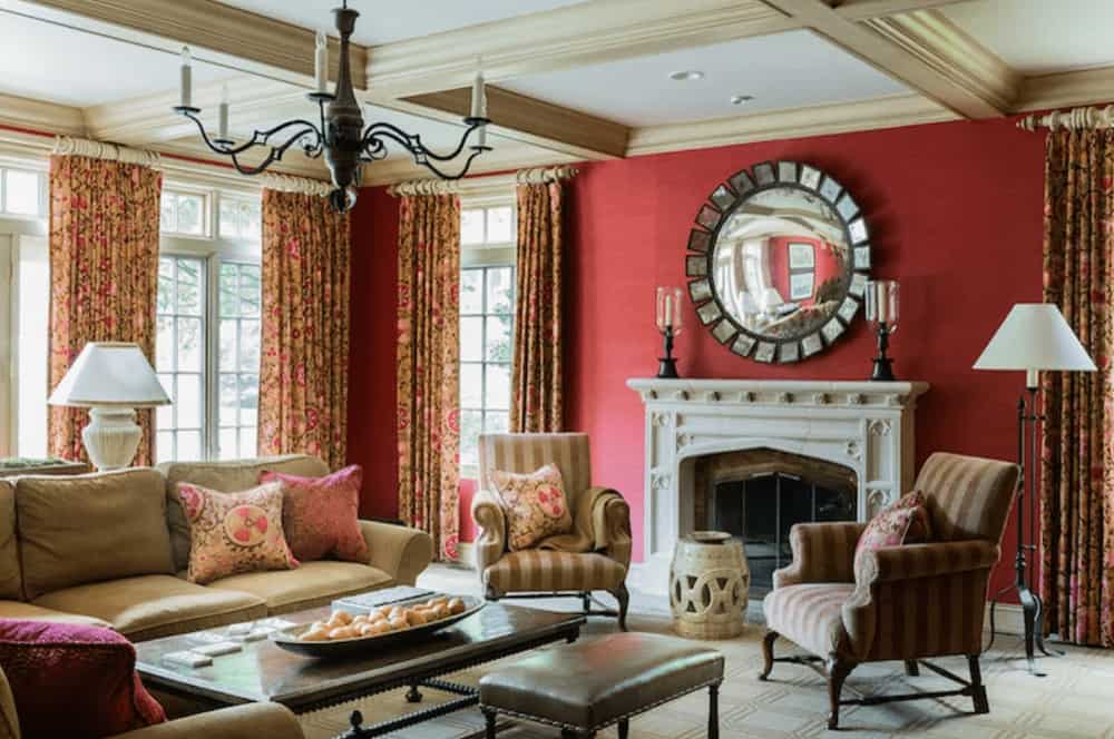 A candle chandelier that hung from the coffered ceiling illuminates this living room boasting comfy seats and a fireplace with candle holders and a concave mirror on top.