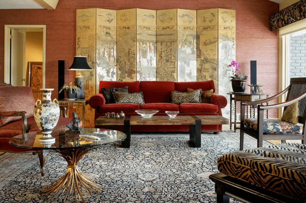 Classic living room with cozy seats and various tables that sit on a floral area rug. It includes a painted screen that sets a classy backdrop to the red sectional sofa.