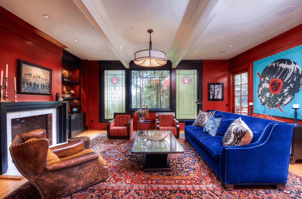 Large blue artwork and gorgeous velvet sofa stand out in this red living room showcasing cozy seats and sleek coffee table illuminated by a drum pendant and recessed ceiling lights. There's a brick fireplace on the side framed with white marble surround and black mantel.