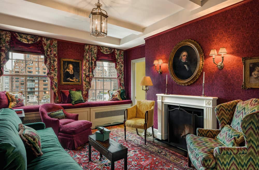 Victorian living room decorated with lovely portraits and a lantern pendant light that hung over the wooden coffee table. It has mismatched seats and a white fireplace covered in a three-panel screen.