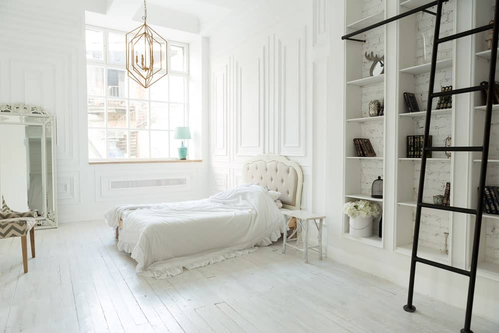 Large primary bedroom with a tall ceiling and white walls. The room has a charming bed setup lighted by a gorgeous ceiling light. The room also offers built-in shelves.
