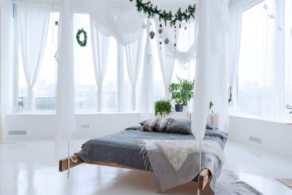 A focused shot at this primary bedroom's stunning bed setup with indoor plants, surrounded by white walls and floors, along with white curtains.
