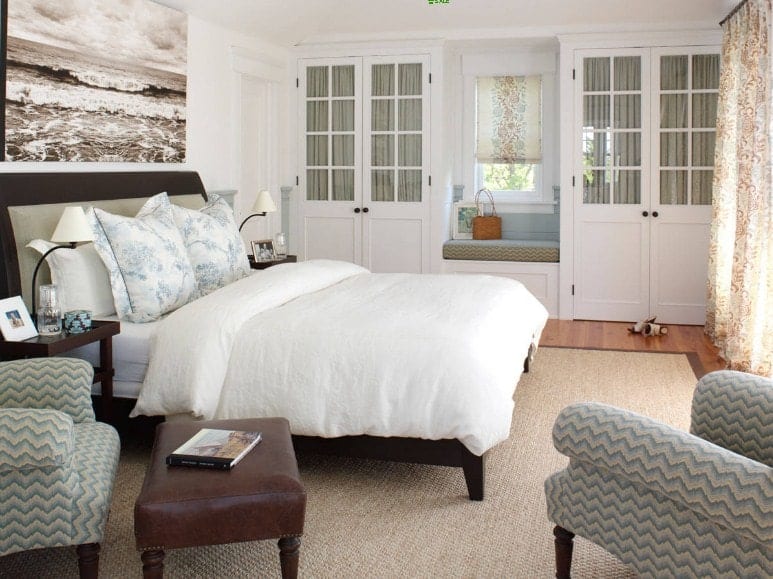 Primary bedroom featuring a large cozy bed along with a sitting area with two beautiful chairs on the side.