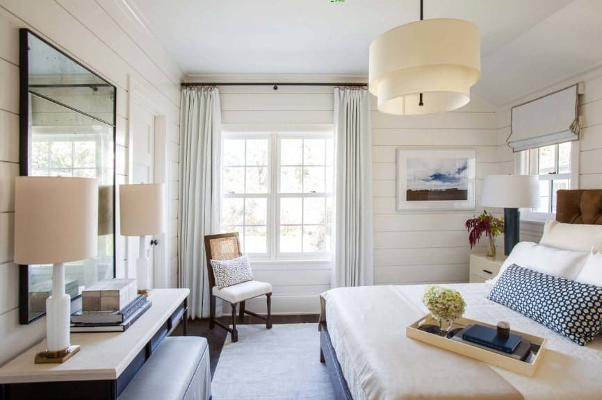 Spacious primary bedroom featuring a large elegant bed along with a built-in desk in front lighted by two table lamps. The room also features a charming ceiling light.