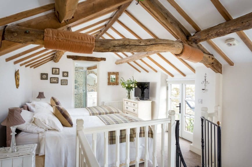 Large primary bedroom featuring white walls and a ceiling with exposed beams. The room boasts two beds with a TV on top of the cabinet.