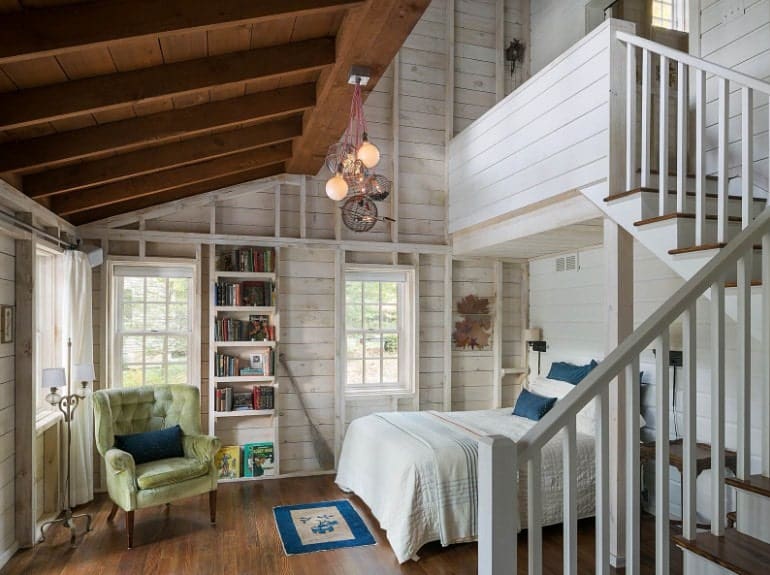 This primary bedroom boasts a wooden ceiling and wooden walls, along with hardwood flooring. It has a staircase leading to the bathroom.