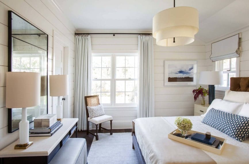 Primary bedroom boasting a classy bed along with a built-in desk in front lighted by table lamps. The room also features a charming ceiling light.