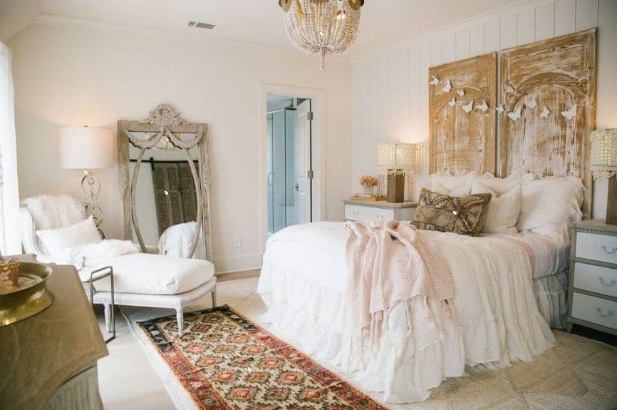 Primary bedroom boasting an elegant bed set lighted by a glamorous chandelier. The room also has its own bathroom area.