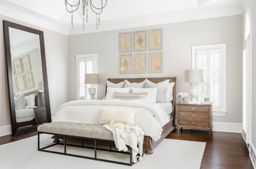 Spacious primary bedroom featuring a large bed with rustic bedside tables topped by classy table lamps. The room features hardwood flooring topped by a white area rug.