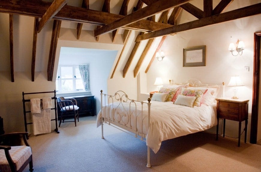 Large primary bedroom featuring carpet flooring and a ceiling with exposed beams. The room offers a nice white bed lighted by wall lights.