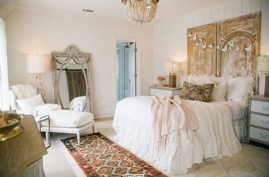Primary bedroom boasting an elegant bed set lighted by two classy table lamps and a glamorous chandelier. The room also has its own bathroom.
