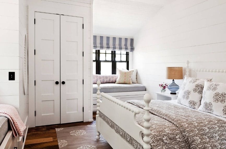 Primary bedroom featuring hardwood flooring, white walls and a white ceiling. The room offers a large classy bed along with a bench seating by the windows.