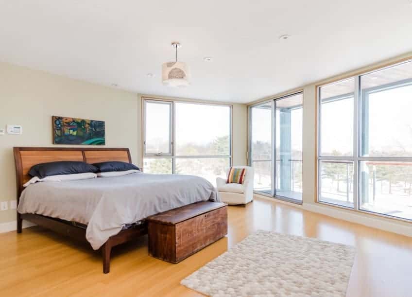 This Scandinavian-Style primary bedroom features glass windows and hardwood floors. There’s a private balcony as well, overlooking the great outdoor views.