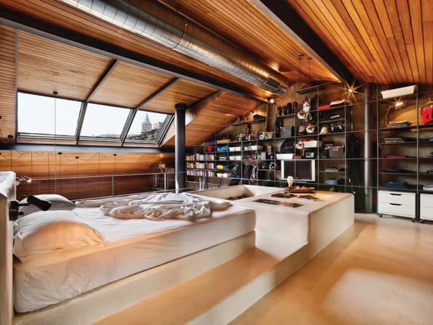 This bedroom has a large wooden cathedral ceiling with a redwood plank finish and accented by the exposed dark wooden beams and the stainless steel vent running in the middle over the white platform bed over the light hardwood flooring.