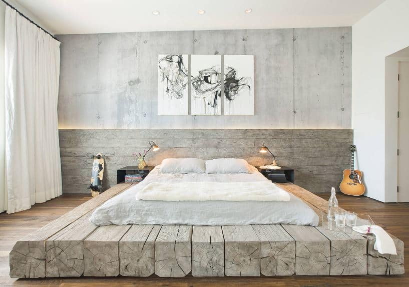 The white cushion is placed on a large platform made of several wooden beams beside each other. This complements the hardwood flooring that matches with the gray concrete wall adorned with framed artworks.