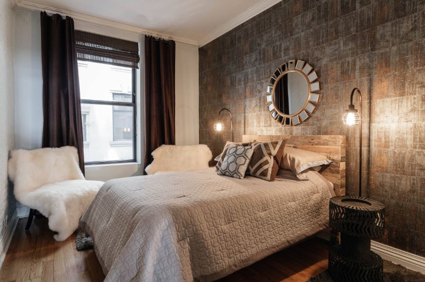 The wall behind the wooden headboard of the traditional bed has a wallpaper with a design that is distinctly industrial-style. This is augmented by a couple of industrial-style lamps peculiar industrial-style bedside tables.