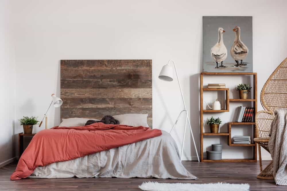 The back-less wooden shelf on the right side of the bed stands out against the white wall. This is also true for the large wooden headboard with a hue that matches that of the hardwood flooring and the bedside table.