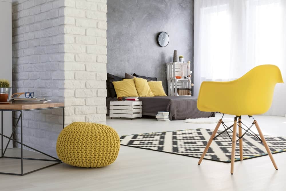 The industrial white flooring is a perfect match for the white stone wall with a brick wall pattern to it. This is brightened by the tall curtained windows that also brighten up the contrasting dark gray bed.