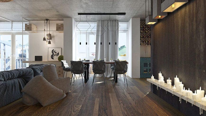 This hallway of dark hardwood flooring and walls with rows of candles leads to a dining area that has the same flooring under a modern row of pendant light that are mounted on the concrete ceiling over the wooden dining table.