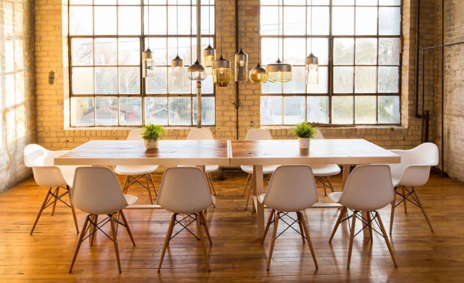 The charming dining room has a relaxing tone to its natural lights that illuminate the hardwood flooring and wooden dining table. This makes the white modern chairs shine brighter and the uniqueness of the pendant lights stand out.