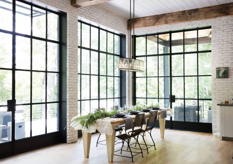The walls of this dining room is dominated by the tall and large glass windows with black frames that matches with the metal chairs of the wooden dining table topped with an elegant crystal pendant light from the high ceiling.