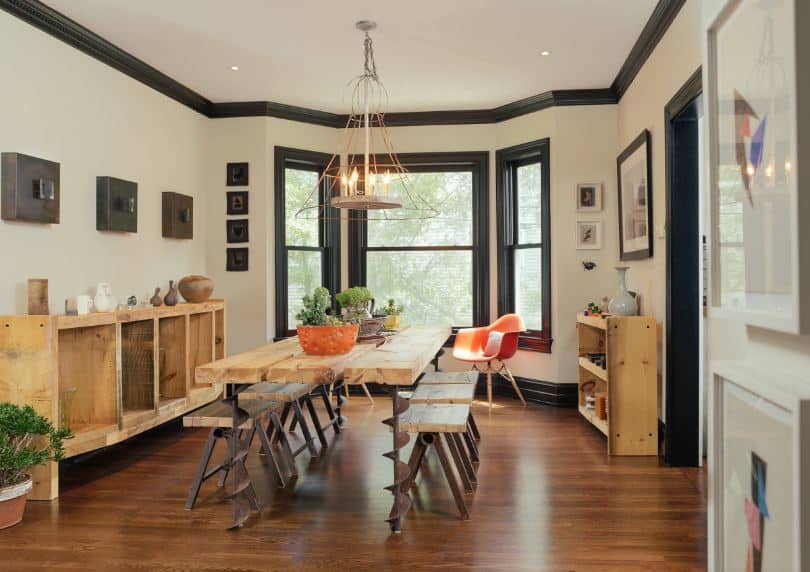 This industrial-style dining room has a slight farmhouse-style to its wooden dining table and matching dining room cabinets and shelves. The dining table has a drill design to its iron legs that match with the benches.