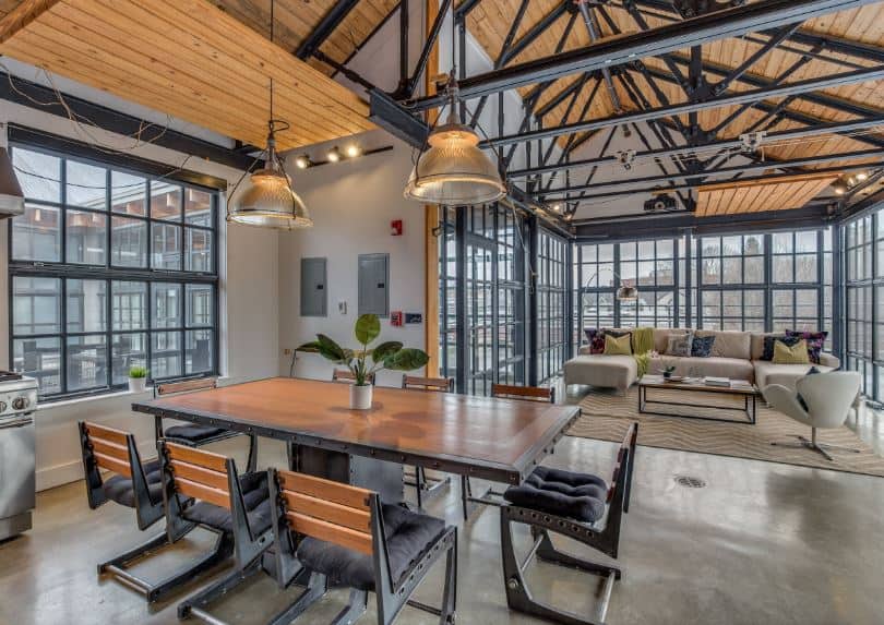 This dining area is part of a great room with a high cathedral ceiling that has exposed metal beams and wooden planks. This is matched with dining set of wooden table and chairs that has dark metal frames.
