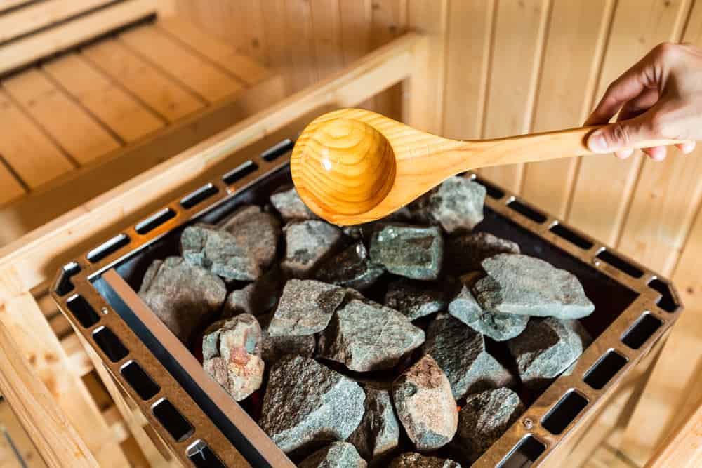 Wood ladle pouring water on hot sauna rocks