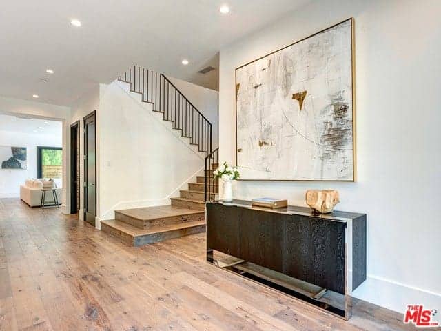 The white walls of this foyer is brightened by the recessed lights of the white ceiling. This is accented with a light hued abstract painting mounted above the dark wooden console table with a cabinet. This bears lovely decors and a flower vase.