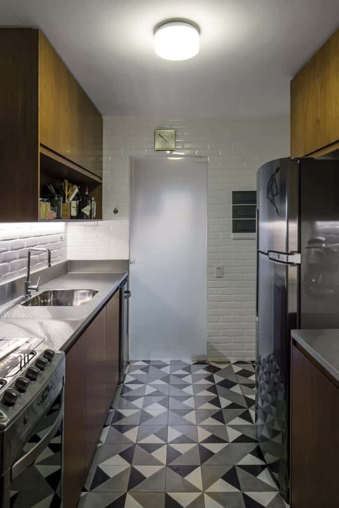 This small kitchen has white wall tiles that are arranged in a brick wall pattern. This is a nice complement to the complex patterned flooring tiles made of white, black and gray triangles. This matches the appliances and the countertops.