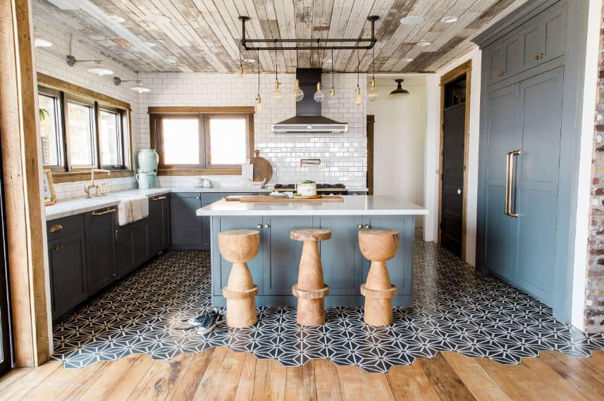 The distressed wooden ceiling is paired with a complex flooring filled with patterns. These are a nice background for the light gray shaker cabinets and drawers of the kitchen island and L-shaped peninsula with white countertops.