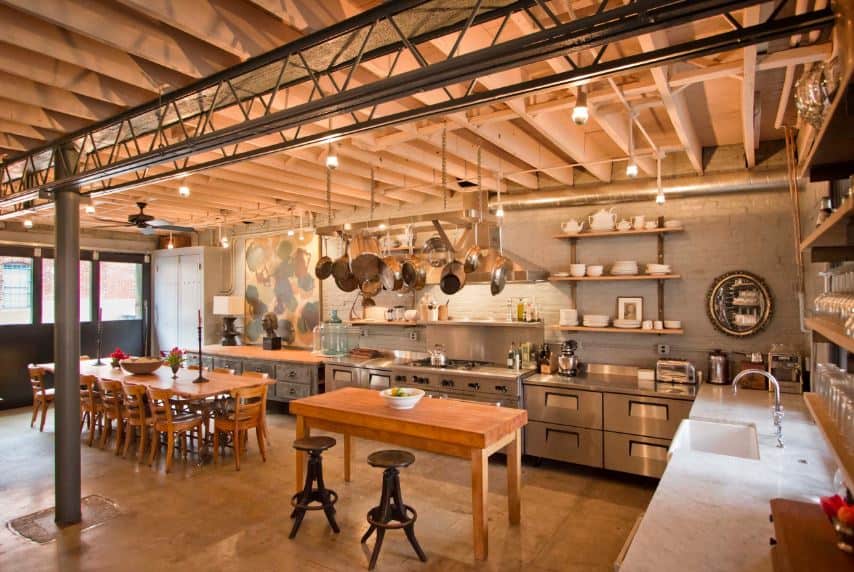 This industrial-style kitchen shares its wide wooden ceiling with the dining area beside it. This wooden ceiling that has exposed wooden beams are supported by a metal column connected to metal trusses above that goes well with the metal peninsula.
