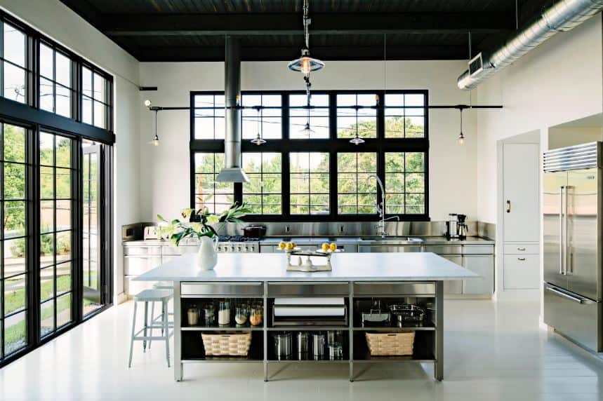 The stainless steel cabinets and shelves of the kitchen island and peninsula matches with the stainless steel appliances as well as with the exposed vents and ducts of the high ceiling that is painted black to match the frames of the glass doors and windows.