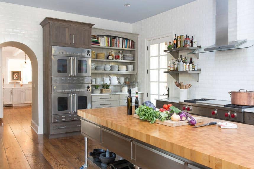 The distressed hardwood flooring of this kitchen is paired with industrial-style cabinets and drawers of the island and peninsula that is made of stainless steel. This goes well with the stainless steel appliances as well as the vent of the cooking area.