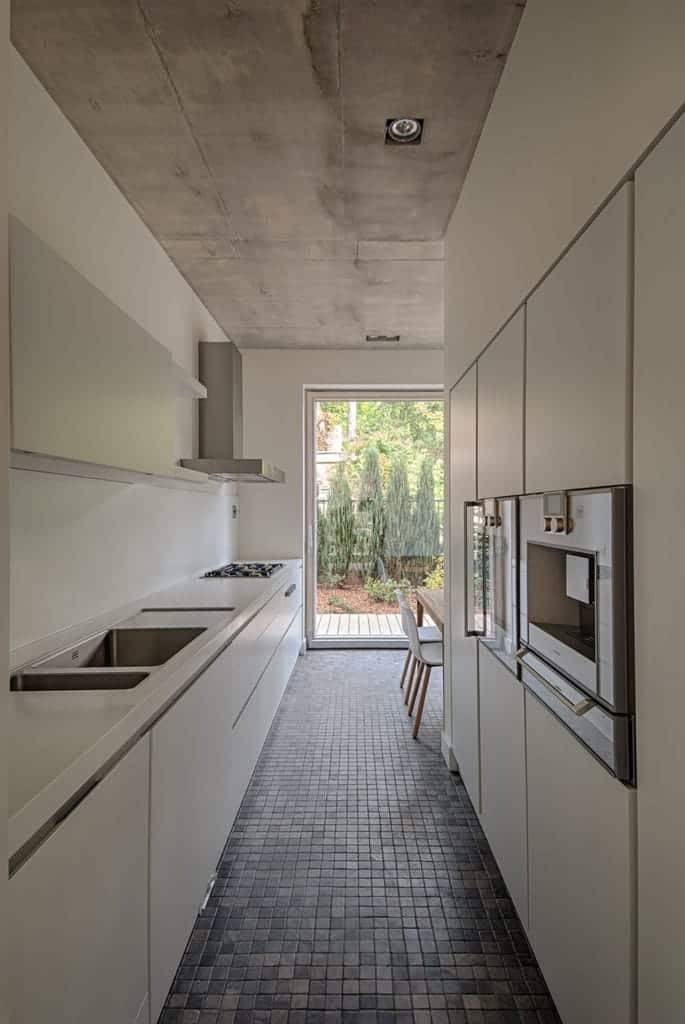 The narrow kitchen has a concrete gray ceiling with recessed lights. This matches with the gray tiles of the floor as well as the stainless steel appliances that stand out against the white modern cabinets and drawers of the peninsula.