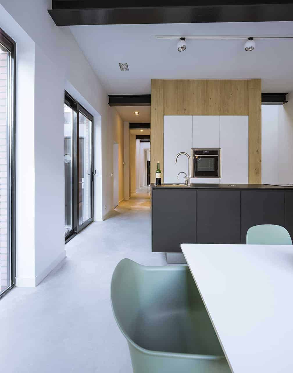 This small and simple kitchen has a dark gray kitchen island with a dark countertop that stands out against the silver faucet but matches with the exposed metal beam of the white ceiling that complements the wooden panel that contains the oven.