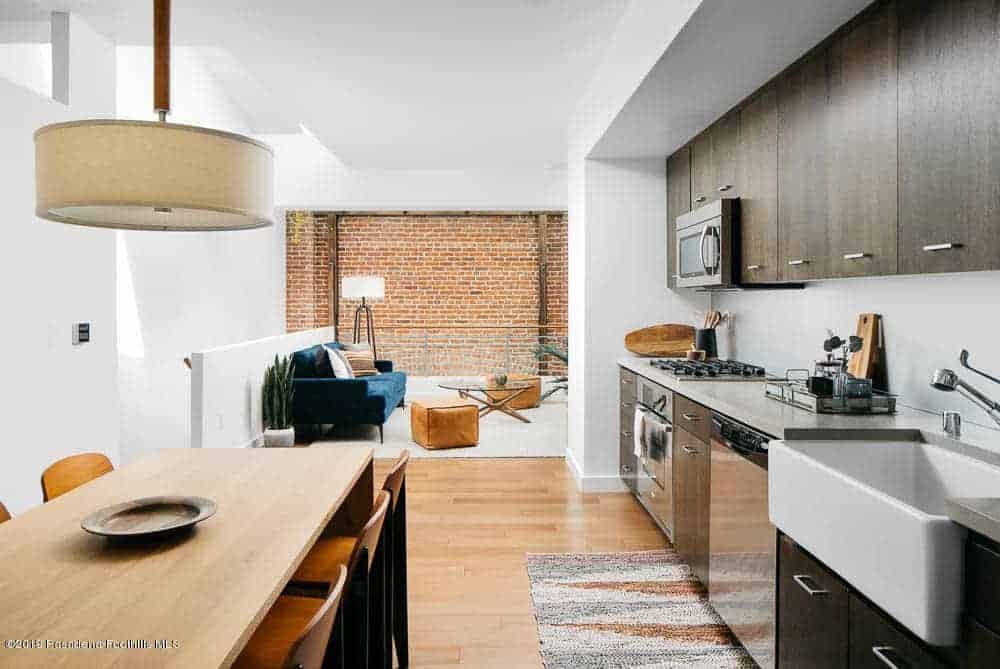 This small kitchen is right beside the informal dining area that has the same wooden table as the hardwood flooring. The dark brown cabinets of the peninsula stands out against the white ceiling and has a nice background of a brick wall.