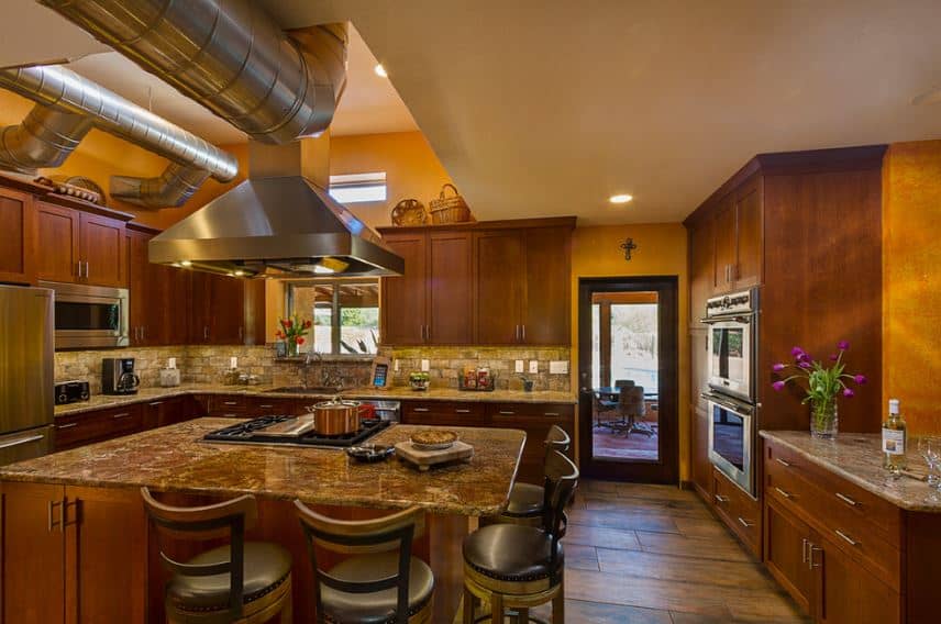 The traditional-style dark wooden shaker cabinets and drawers of this charming kitchen are contrasted by the stainless steel exposed vents and ducts of the ceiling that matches with the stainless steel appliances.