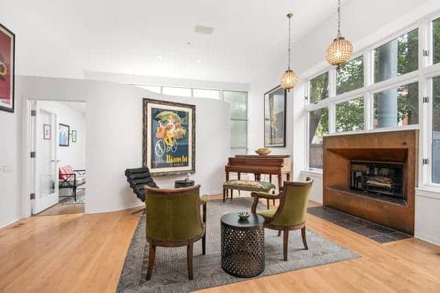 The bright white walls and ceiling of this industrial-style living room is augmented by the hardwood flooring and the unique fireplace that is embedded with a wooden frame that brings warmth to the green velvet armchairs.