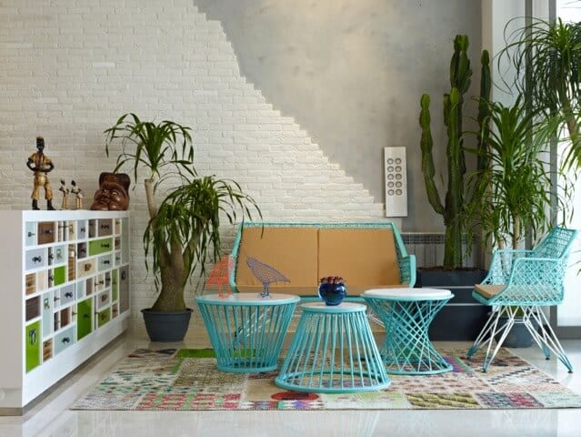 This industrial-style living room has a cheery demeanor thanks to the light green set of furniture over a colorful patterned area rug. This is given a background of gray concrete that fades into a white stone wall.