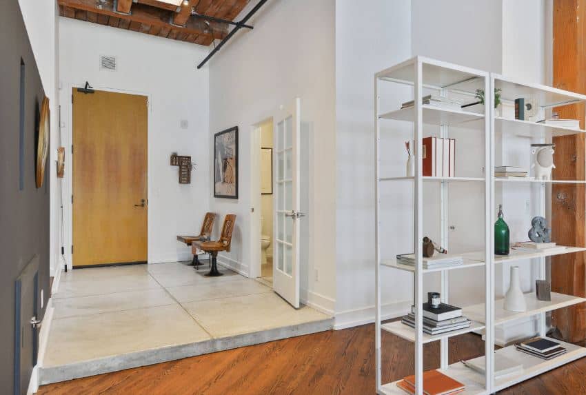 This wooden main door opens to a foyer that has a concrete flooring that complements the white walls and the high wooden ceiling with exposed wooden beams, wires and tubing for that distinctive industrial feel that matches with the rest of the home.