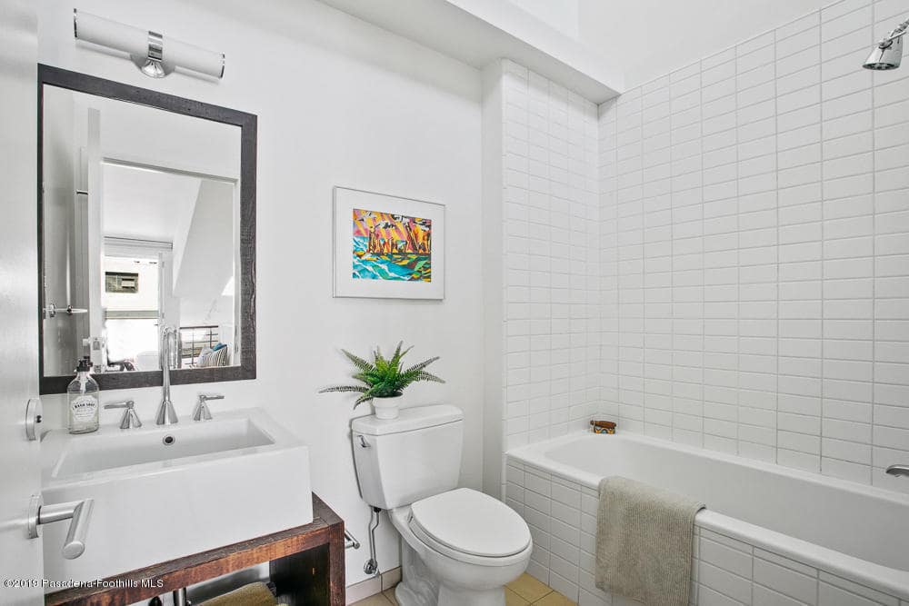 This simple bathroom has a white ceiling that matches with the white walls blending with the white porcelain toilet and the floating white sink with exposed pipes underneath. These pipes matches with the faucet and the wall-mounted lamp above the mirror.