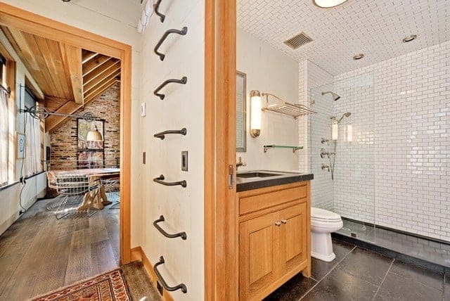This bathroom has the same white tiles on its ceiling as the walls of the glass-enclosed shower area. These white tiles are arranged in a brick wall pattern that provides a nice complexity to the dark flooring and beige vanity wall adorned with a mirror and modern wall lamp.