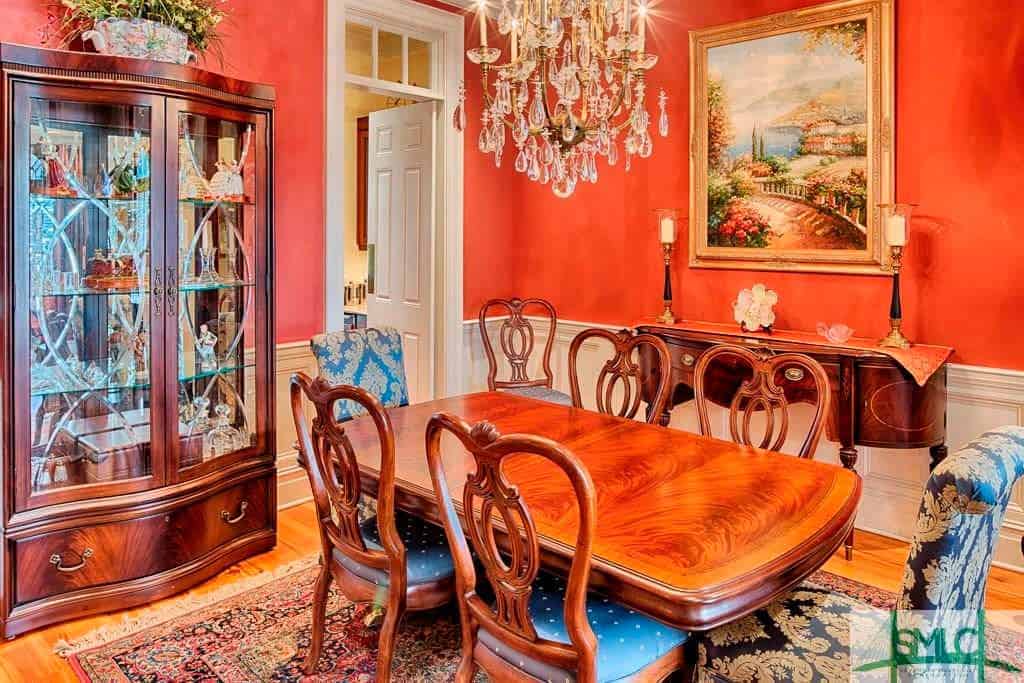 The orange walls of this elegant and chic dining room sets a nice background for the traditional elements of the wooden dining table and chairs that match with the dining room cabinet with glass panels that pair nicely with the crystal chandelier.